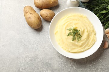 Tasty mashed potato in bowl, spices, herbs and raw vegetables on grey textured table, flat lay. Space for text