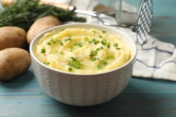 Tasty mashed potato with green onion in bowl and raw vegetables on light blue wooden table, closeup