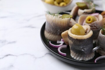 Delicious herring rolls with olives, pickles, dill and onion on light marble table, closeup. Space for text