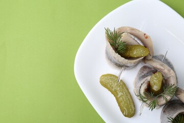 Delicious herring rolls with pickles and dill on light green table, top view. Space for text