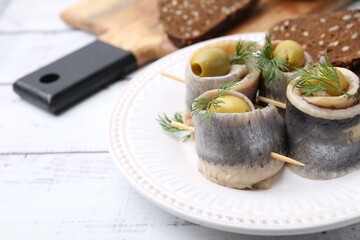 Delicious herring rolls with olives, dill and bread on white wooden table, closeup. Space for text