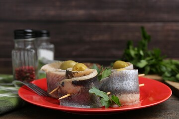 Delicious herring rolls with olives and parsley on wooden table, closeup