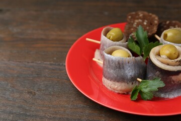 Delicious herring rolls with olives, parsley and bread on wooden table, closeup. Space for text