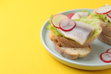 Tasty sandwiches with herring, radish and lettuce on yellow background, closeup. Space for text