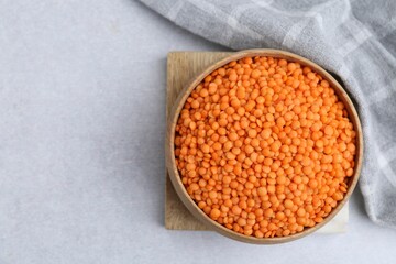 Red lentils in bowl on light table, top view. Space for text