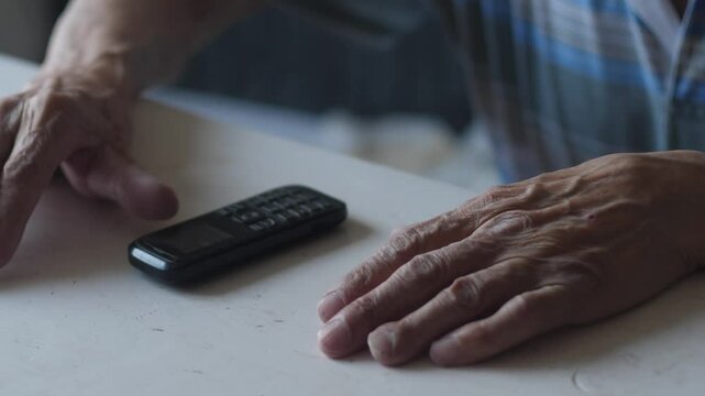 Hands of elderly man using vintage button mobile phone while sitting at table, pensioner making phone call with retro keypad device