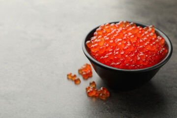 Tasty red caviar in bowl on grey table, closeup. Space for text