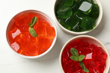 Different jelly cubes in bowls on white marble table, flat lay