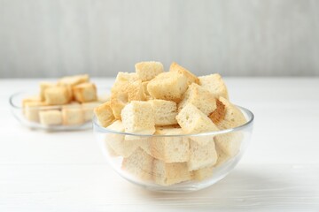 Delicious crispy croutons on white wooden table, closeup