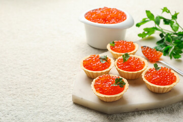 Tartlets with red caviar and parsley on beige table, closeup. Space for text