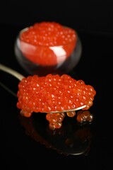 Red caviar on black mirror surface, closeup