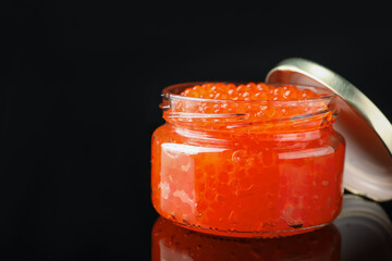 Red caviar on black mirror surface, closeup. Space for text