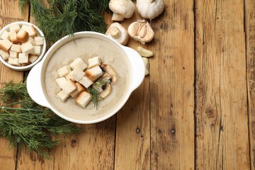 Delicious mushroom cream soup with croutons, dill and ingredients on wooden table, flat lay. Space for text
