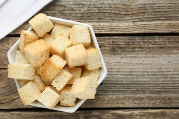 Tasty crispy croutons in bowl on wooden table, top view. Space for text