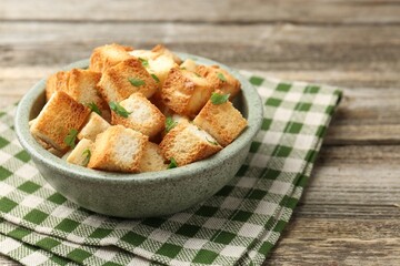 Tasty crispy croutons with cut parsley in bowl on wooden table, closeup
