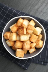 Tasty crispy croutons in bowl on dark textured table, top view