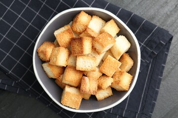 Tasty crispy croutons in bowl on dark textured table, top view