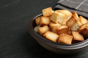 Tasty crispy croutons in bowl on dark textured table, closeup. Space for text