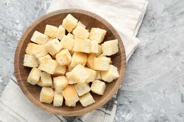 Tasty crispy croutons in bowl on grey textured table, top view