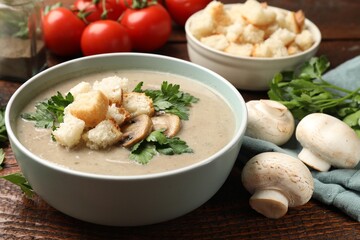 Delicious mushroom cream soup with croutons, parsley and ingredients on wooden table, closeup