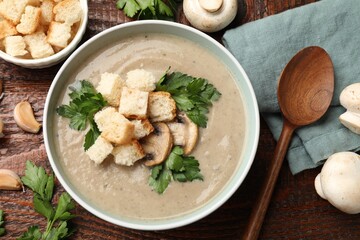 Delicious mushroom cream soup with croutons, parsley, ingredients and spoon on wooden table, flat lay