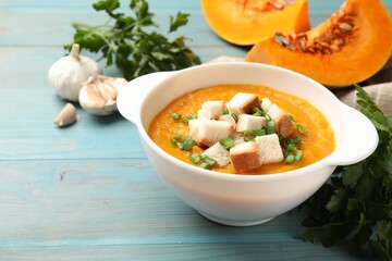 Tasty pumpkin cream soup with croutons, green onion and parsley on light blue wooden table, closeup