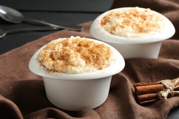 Delicious rice pudding with cinnamon in bowls and spoons on black wooden table, closeup