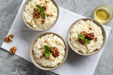 Delicious rice pudding with walnuts, mint and honey on grey table, flat lay