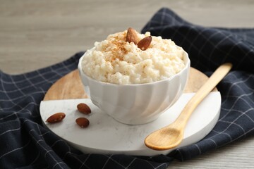 Delicious rice pudding with cinnamon, almonds and spoon on wooden table, closeup