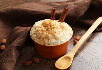 Delicious rice pudding with cinnamon, almonds and spoon on wooden table, closeup