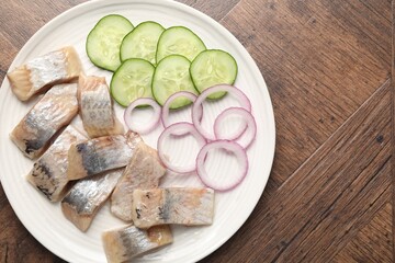 Pieces of delicious herring, onions and cucumber slices on wooden table, top view. Space for text