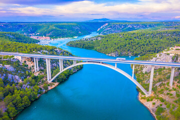 Drone image of the reinforced concrete arch Sibenik Bridge spanning Sibenik Bay near the mouth of the Krka River, with the scenic town of Skradin visible in the distance behind the bridge
