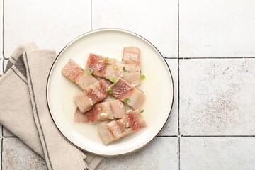 Pieces of delicious herring with green onions on tiled table, top view