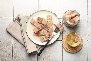 Pieces of delicious herring with green onions on tiled table, flat lay