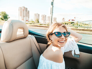 Portrait of young beautiful and smiling hipster female in convertible car. Carefree woman driving...