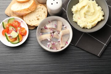 Delicious herring pieces with onions served on black wooden table, flat lay