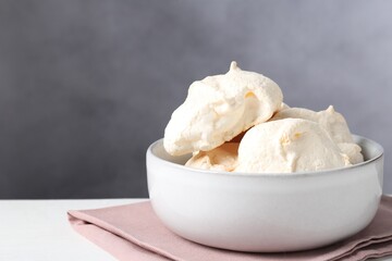 Delicious homemade meringue cookies in bowl on light table against gray background, space for text