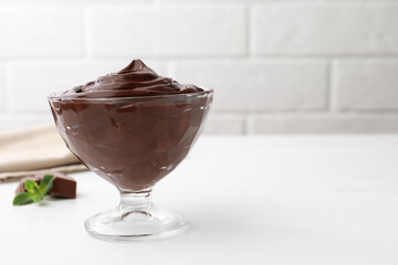 Delicious chocolate pudding in dessert bowl on white table against brick wall, closeup. Space for...
