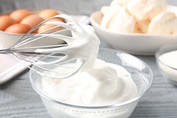 Whisk with whipped cream and other ingredients on gray table, closeup. Cooking meringue cookies