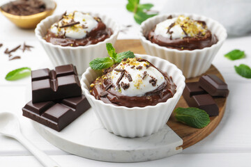Tasty pudding with whipped cream in bowls and pieces of chocolate on white wooden table, closeup