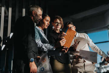 A diverse group of business people analyzing documents and data charts in a modern office. They demonstrate teamwork, communication, and focus, using digital devices to enhance their project planning.