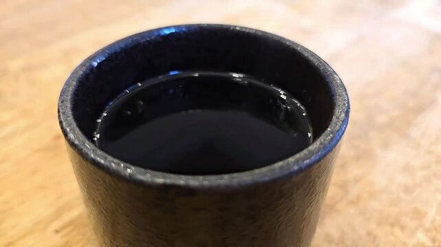 Black Japanese tea bowl filled with hot tea and smoke rising above cup. Ceramic teacup placed on wooden table. Drinking fragrant tea for health. Aroma in hot tea helps reduce risk of stroke,body relax