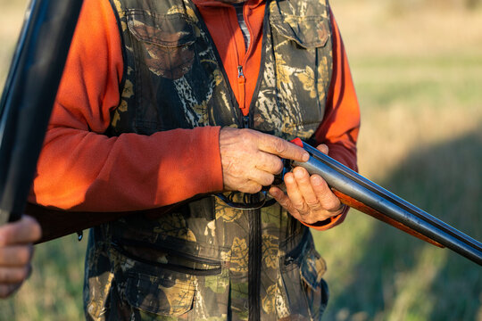 Mature hunter man holding a shotgun and walking through a field
