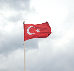 State flag of Turkey with star and crescent waving on flagpole in overcast day against strong gray rainy clouds