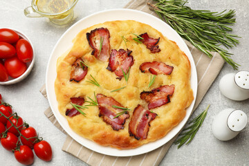 Delicious focaccia bread with bacon, rosemary, tomatoes and oil on light grey table, flat lay