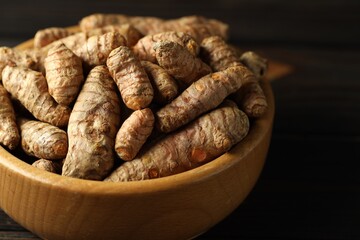 Tumeric rhizomes in bowl on wooden table, closeup