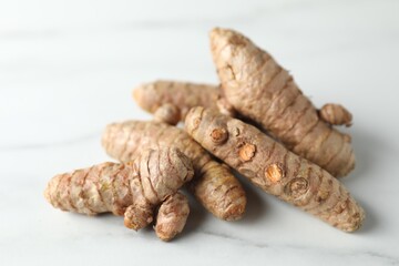 Pile of raw turmeric roots on white marble table, closeup