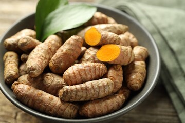 Tumeric rhizomes with leaves in bowl on table, closeup