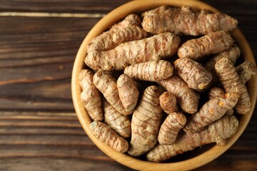 Tumeric rhizomes in bowl on wooden table, top view