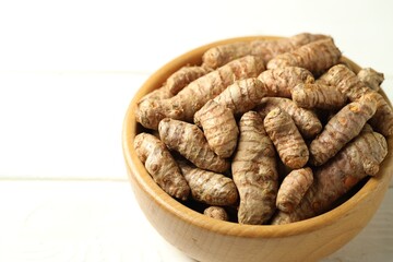 Tumeric rhizomes in bowl on white wooden table, closeup